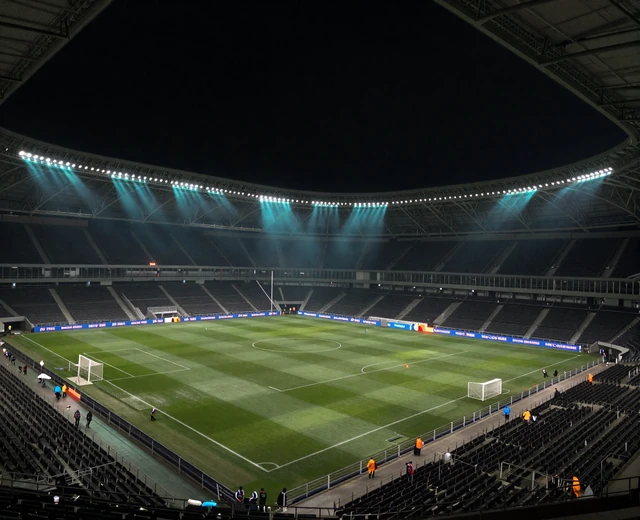 Dunkles Fu&szlig;ballstadion bei Nacht mit t&uuml;rkisem Flutlicht und Bandenwerbung als Symbol f&uuml;r das Sponsoring